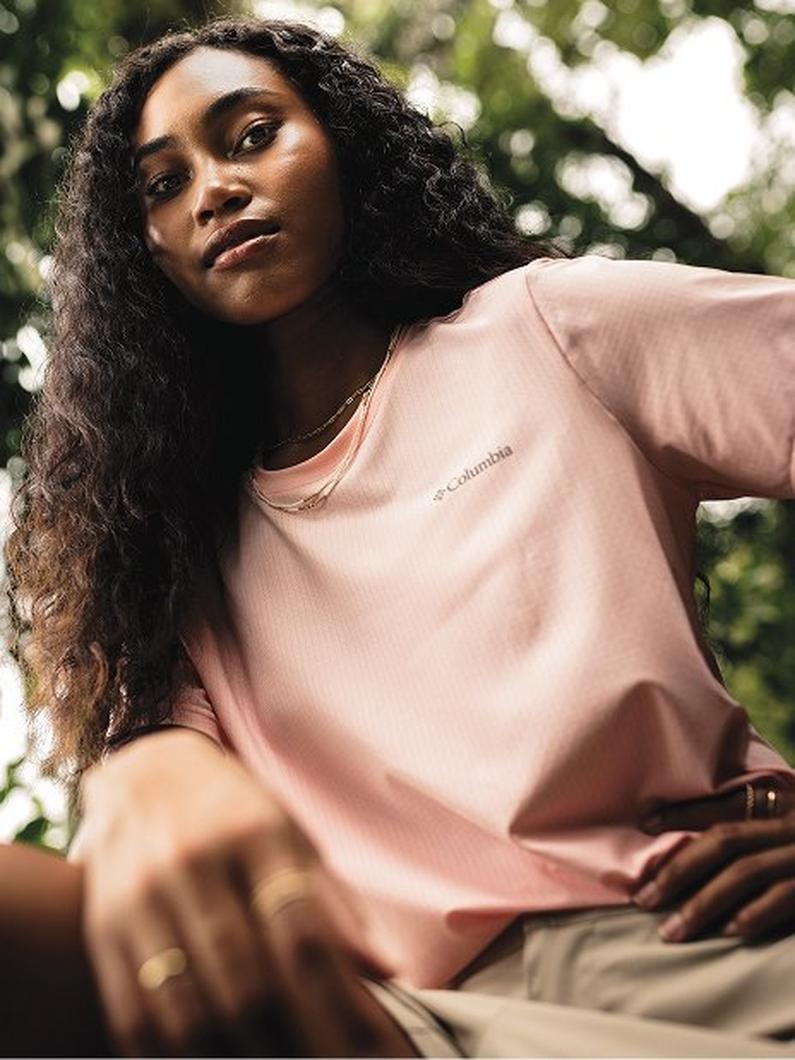 Woman with long curly hair wearing a peach-colored crew neck t-shirt outdoors.