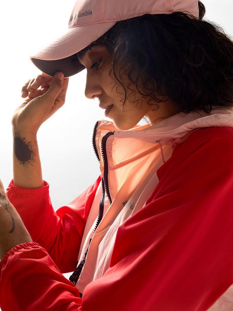 Person wearing pink cap and red and pink color-block jacket adjusting their hat while looking down.