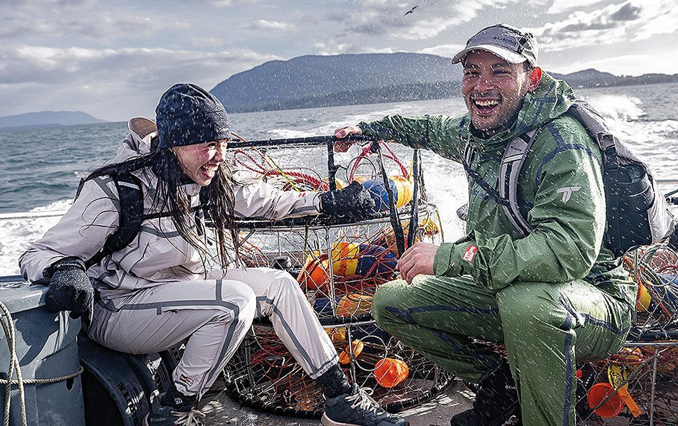 Two peope in full rain gear in the back of a boat being splashed with water