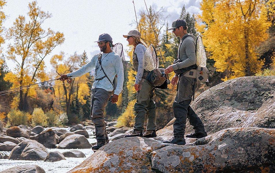 Three people wearing fishing waders prepare to enter a creek with their fly rods.