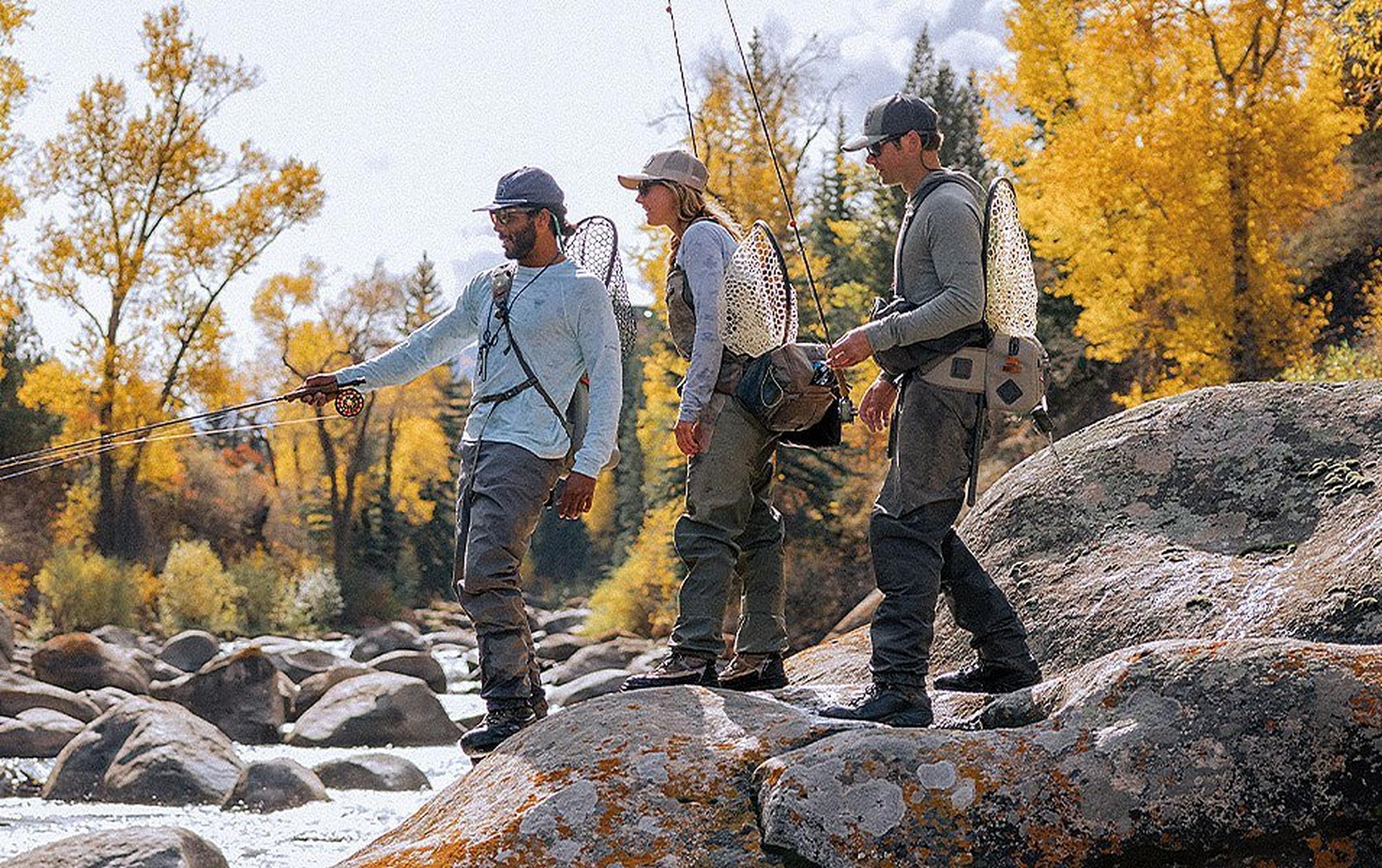 Group of people fly fishing from rocky boulders along a river
