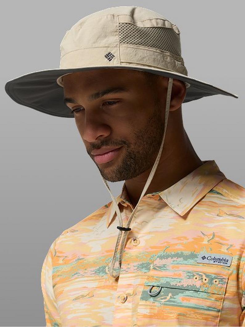 Man wearing a tan wide-brimmed bucket hat with mesh panel and a colorful patterned short-sleeve shirt.