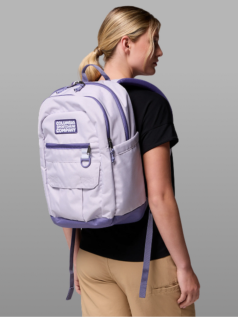 A woman facing away from the camera, wearing a purple backpack.