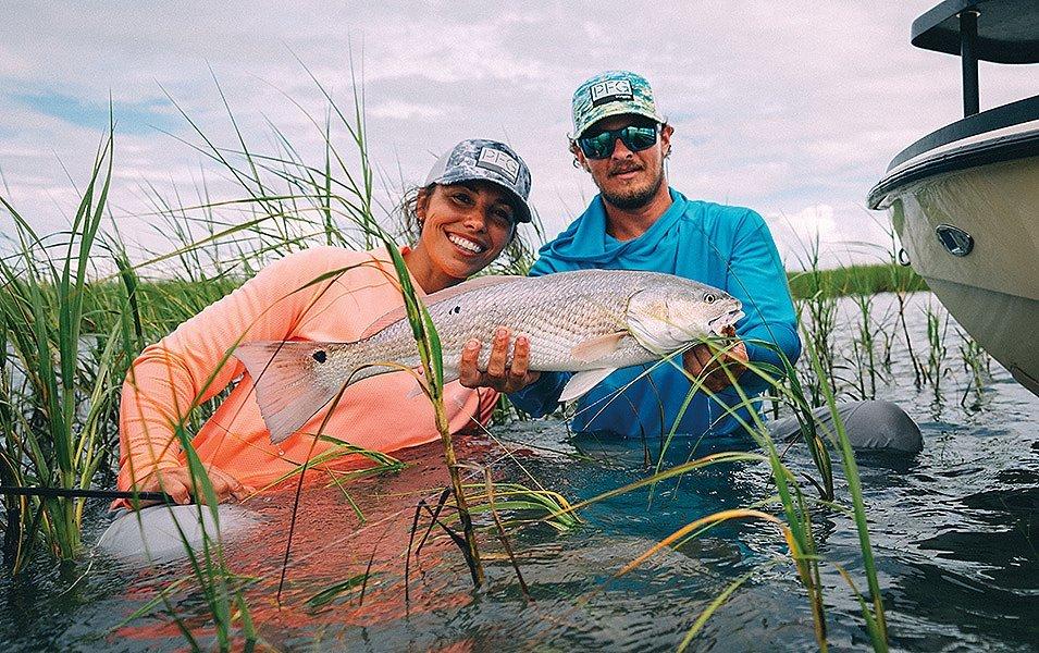 A man and woman wearing Columbia PFG apparel holding a large fish in a marshy waterway. 