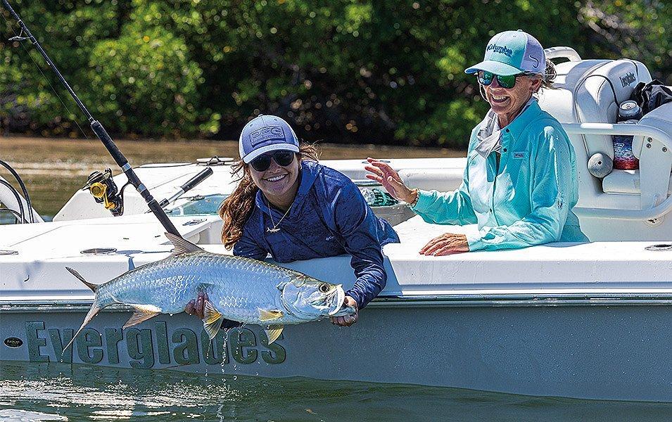 Two women wearing Columbia PFG apparel releasing a large fish from the edge of a fishing boat. 