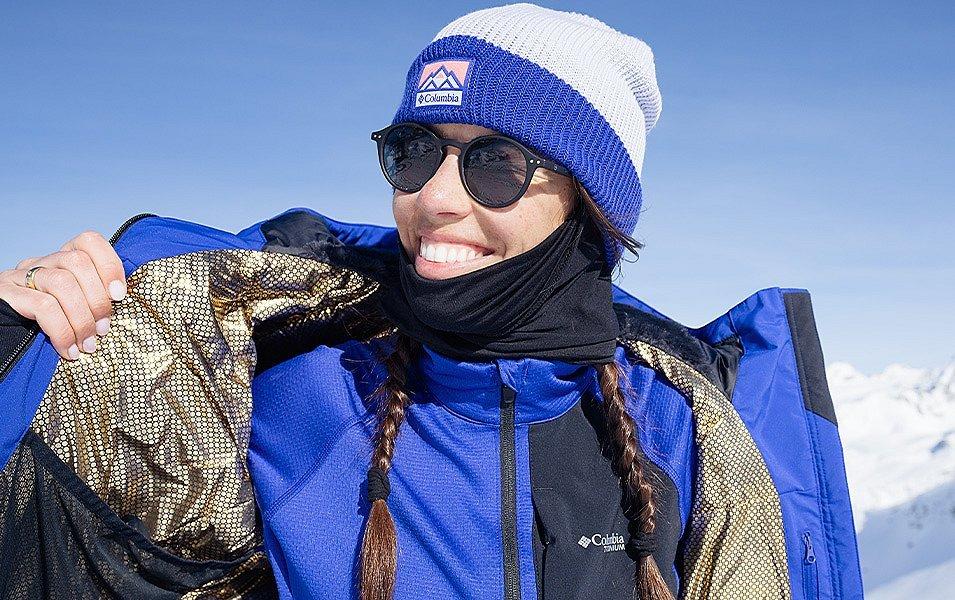 A female skier smiles as she dons a warm winter jacket.  