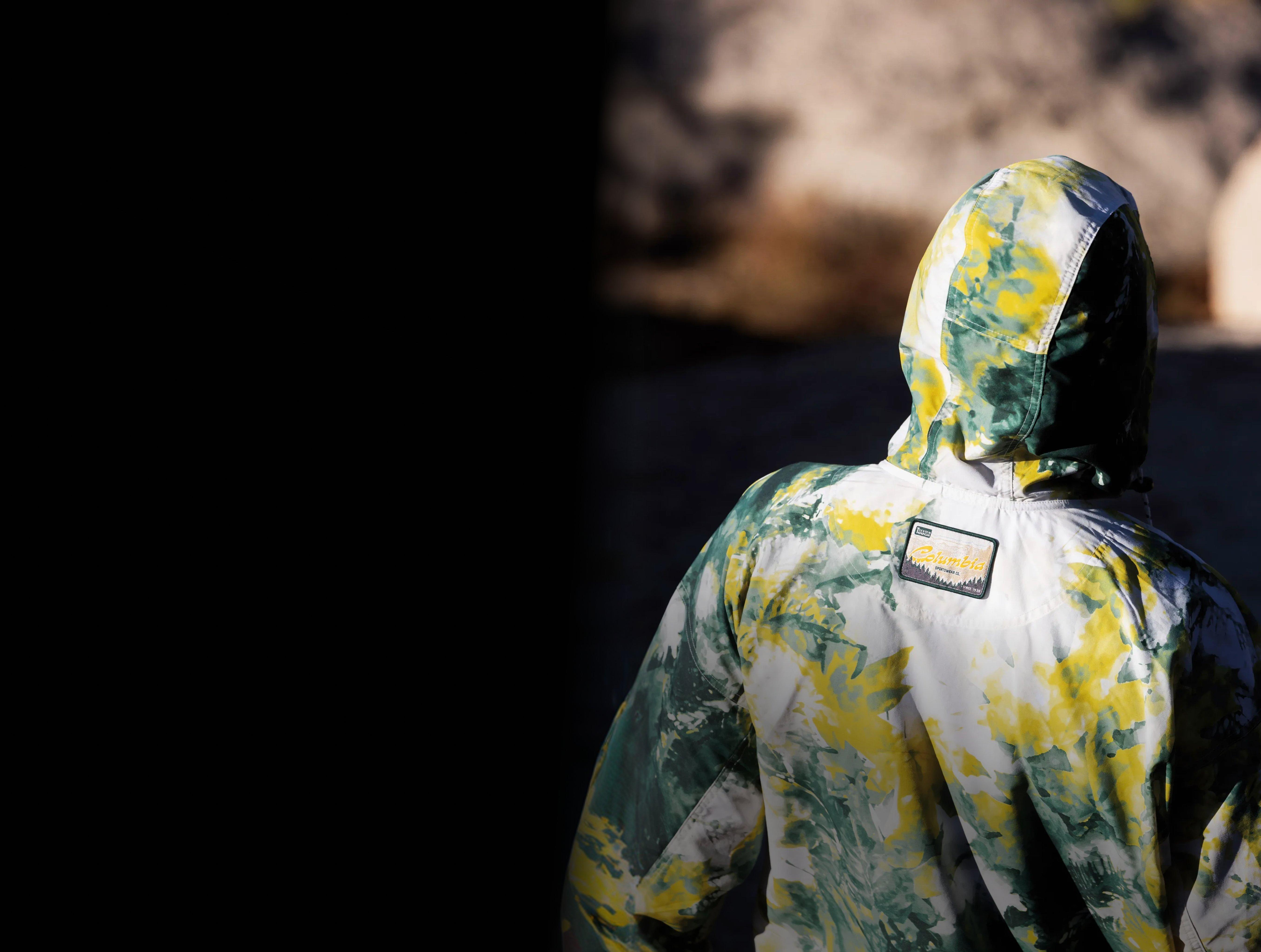 Person wearing a hooded jacket with yellow and green tie-dye pattern, viewed from behind.