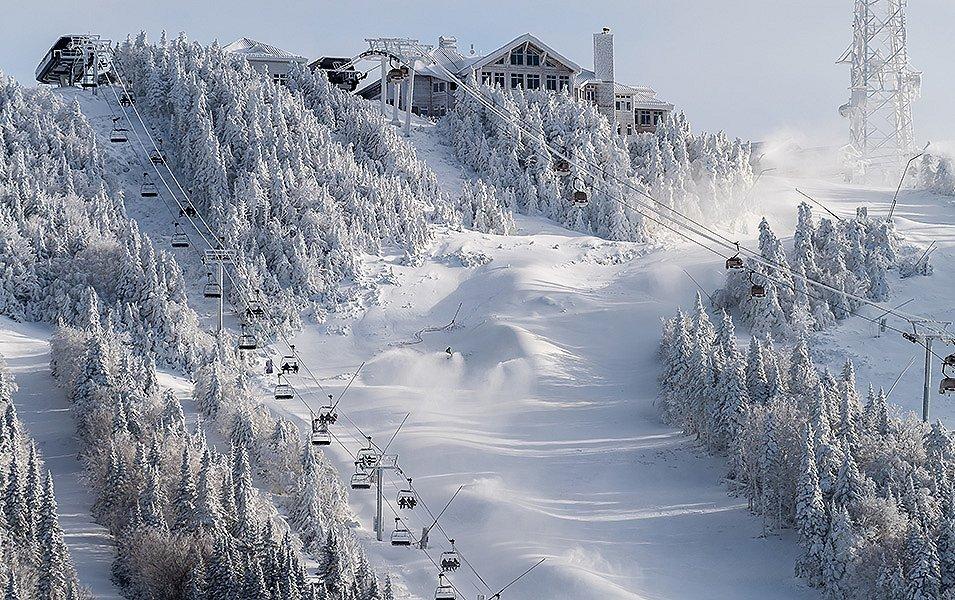 Two chair lifts snake up a snow-covered mountain. At the top is a ski lodge.  