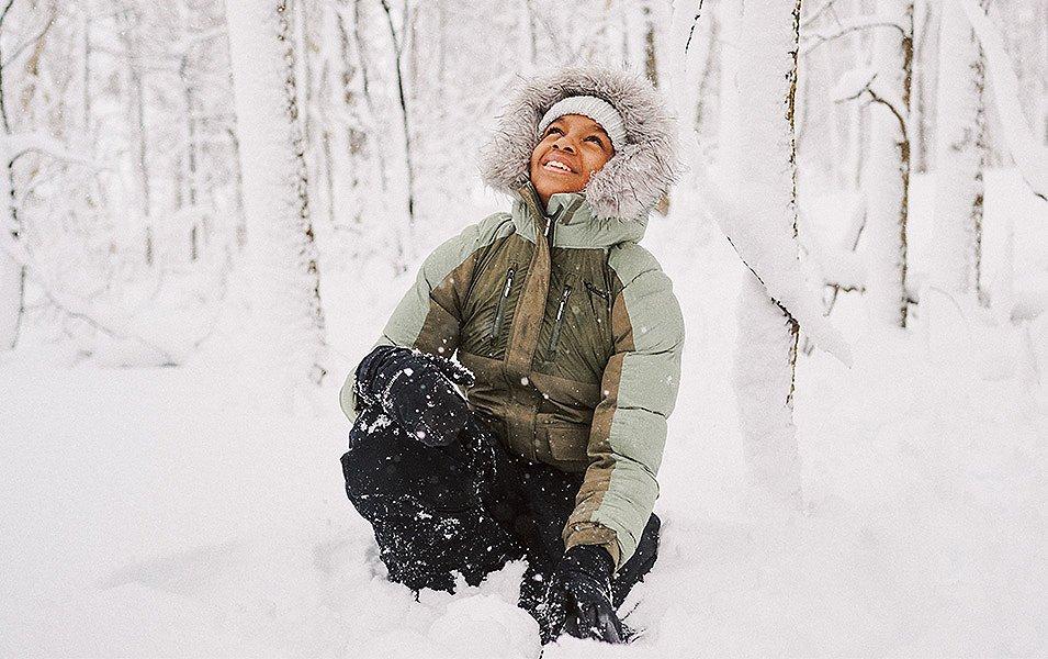 A person with big puffy jacket and faux fur lined hood enjoys playing in the deep snow.
