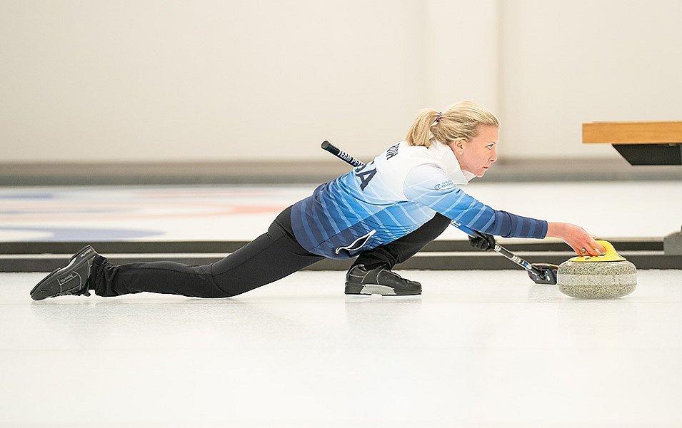 A woman holds a broom in one hand and the stone in the other as she focuses on the game.
