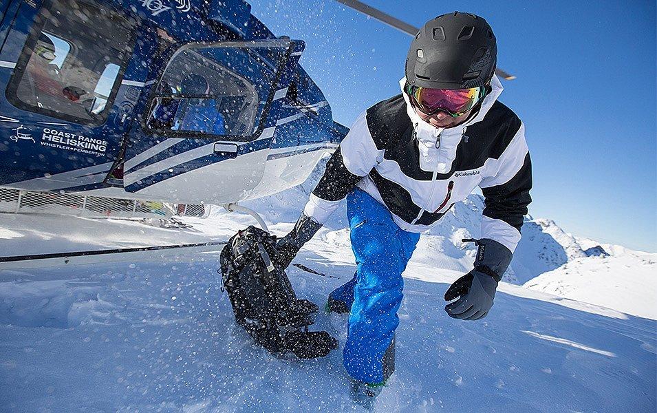 A skier crouches low, following safety protocol, as she exits the helicopter onto a snowy mountainside.