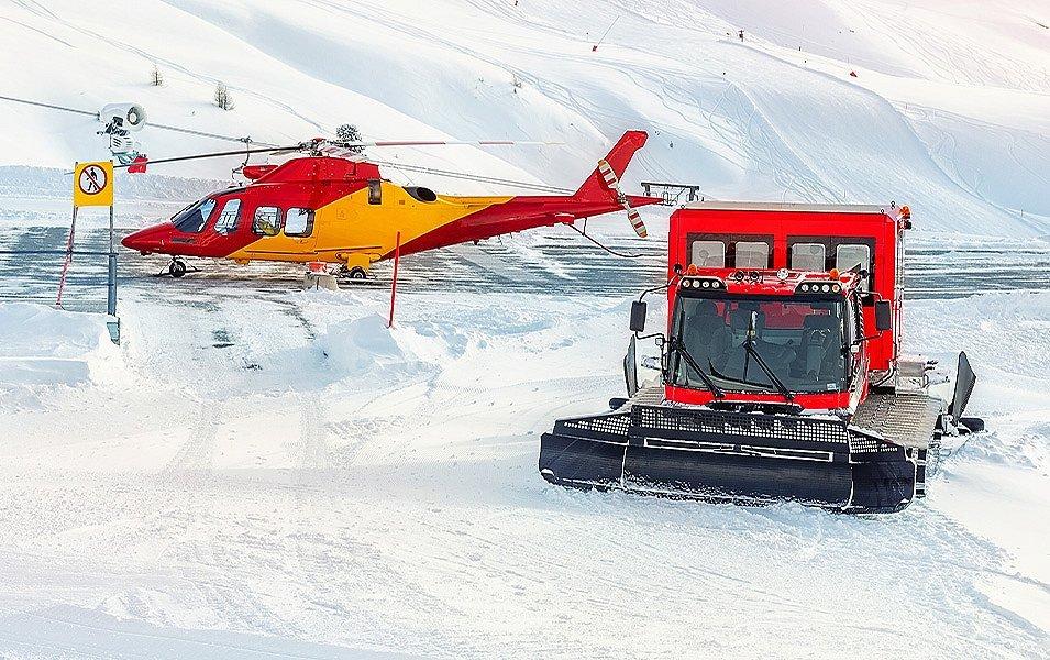 A helicopter and snowcat are at the ready to deliver skiers and snowboarders to the top of a backcountry run.