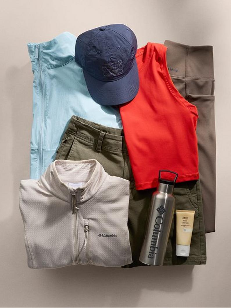 Flat lay of outdoor apparel including fleece jackets, pants, baseball cap, water bottle, and skincare tube.