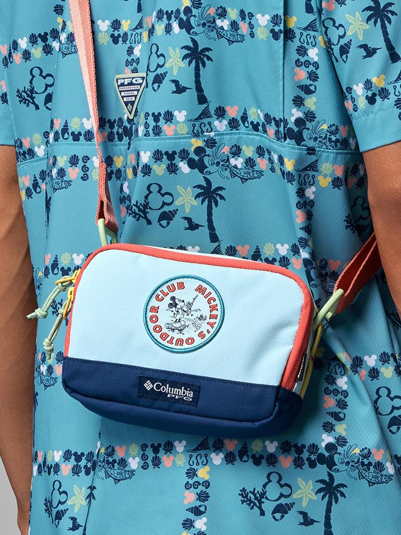Light blue crossbody bag with coral trim worn over a turquoise shirt featuring tropical print.