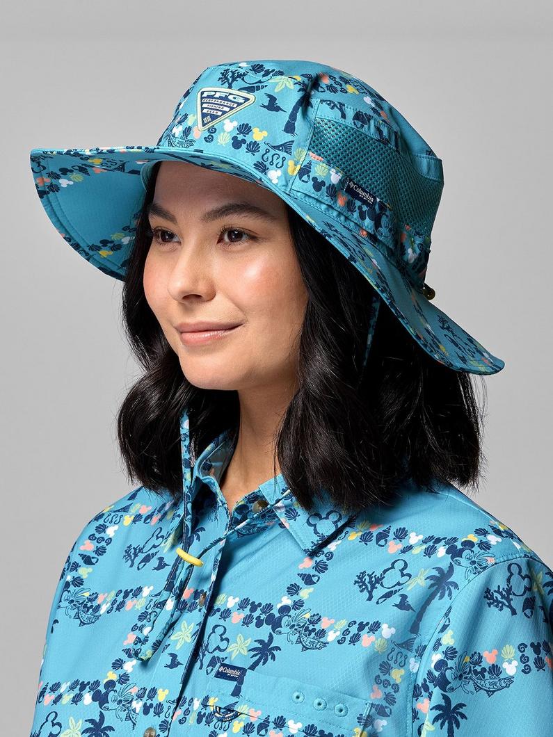 Woman wearing turquoise wide-brimmed sun hat and matching shirt with tropical floral print pattern.