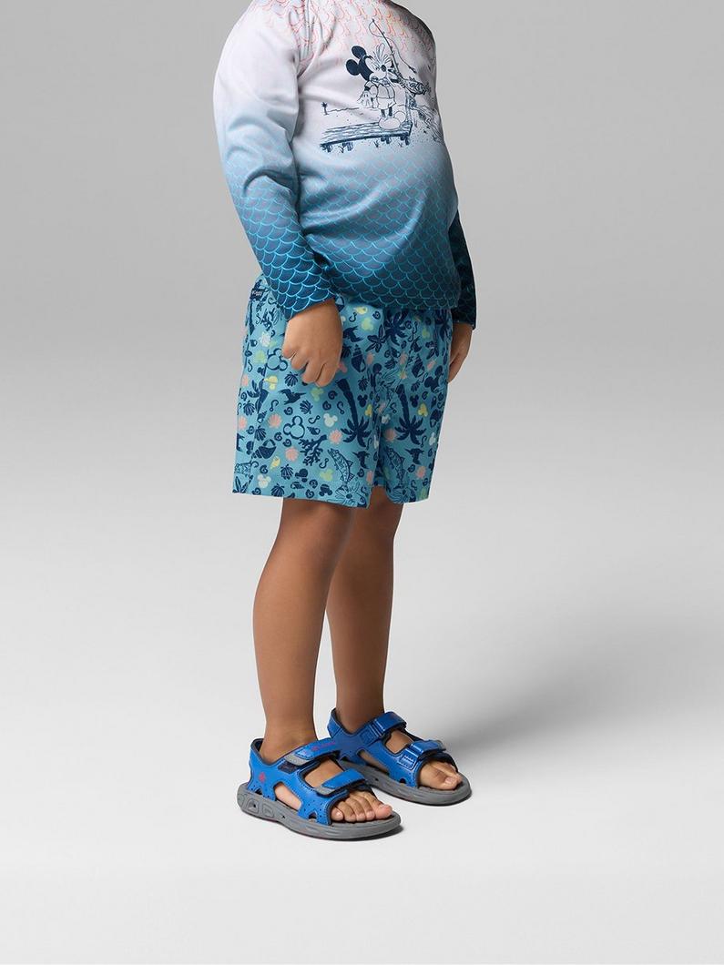 Child wearing ombre long-sleeve shirt with character graphic and blue ocean-themed shorts with sandals.