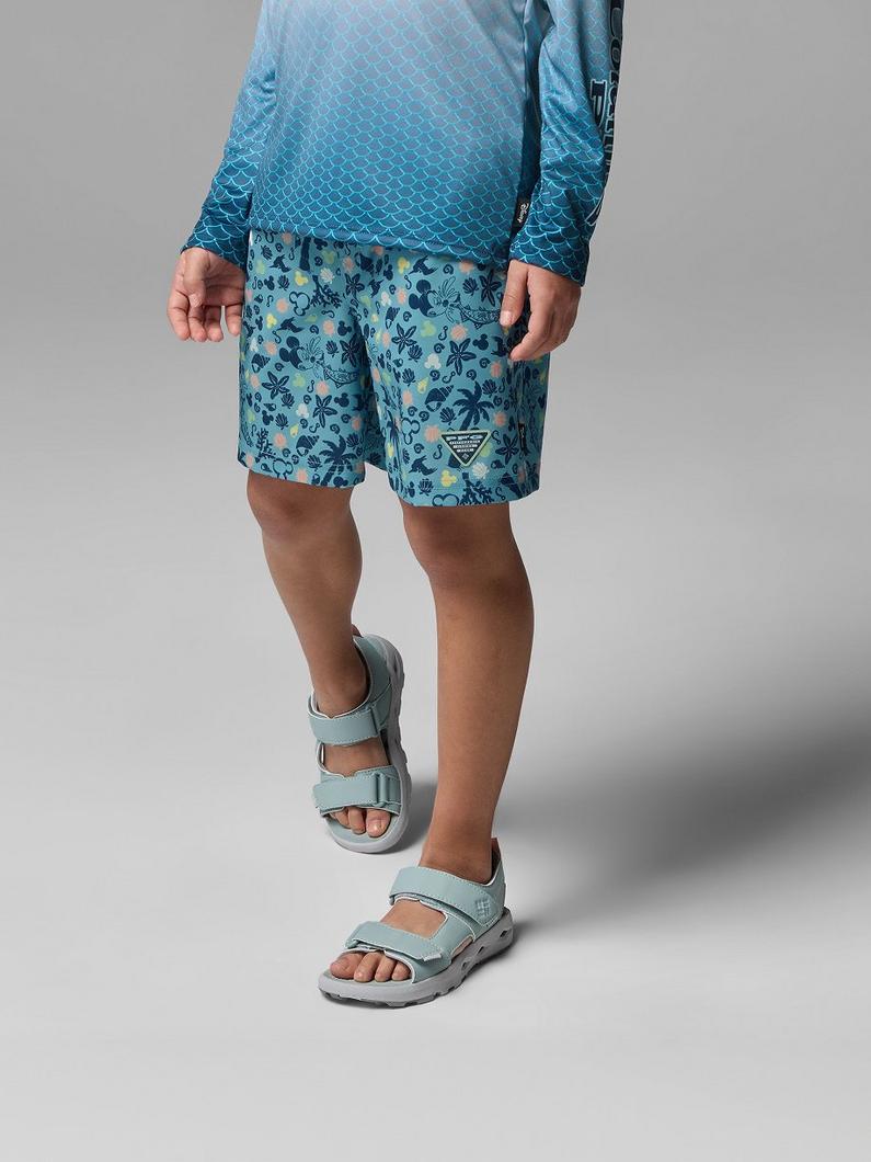Child wearing blue fish-scale pattern long-sleeve shirt and floral print shorts with light blue sandals.