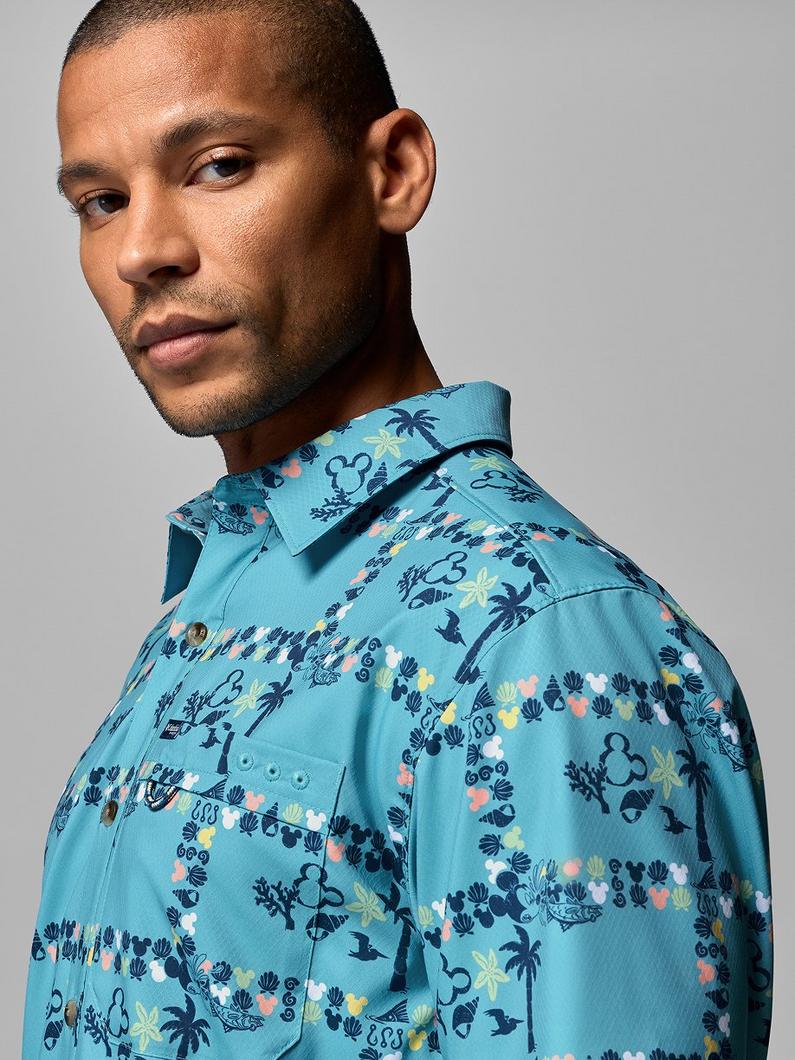 Man wearing a turquoise button-up shirt with tropical palm tree and floral print pattern.