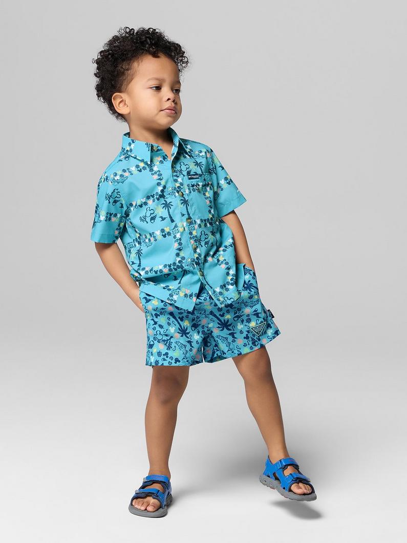 Child wearing turquoise tropical print shirt and matching shorts with hand in pocket.