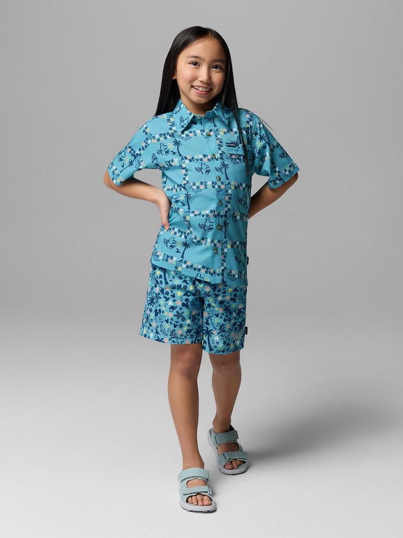 Girl smiling wearing turquoise floral print short-sleeve shirt and matching shorts with sandals.