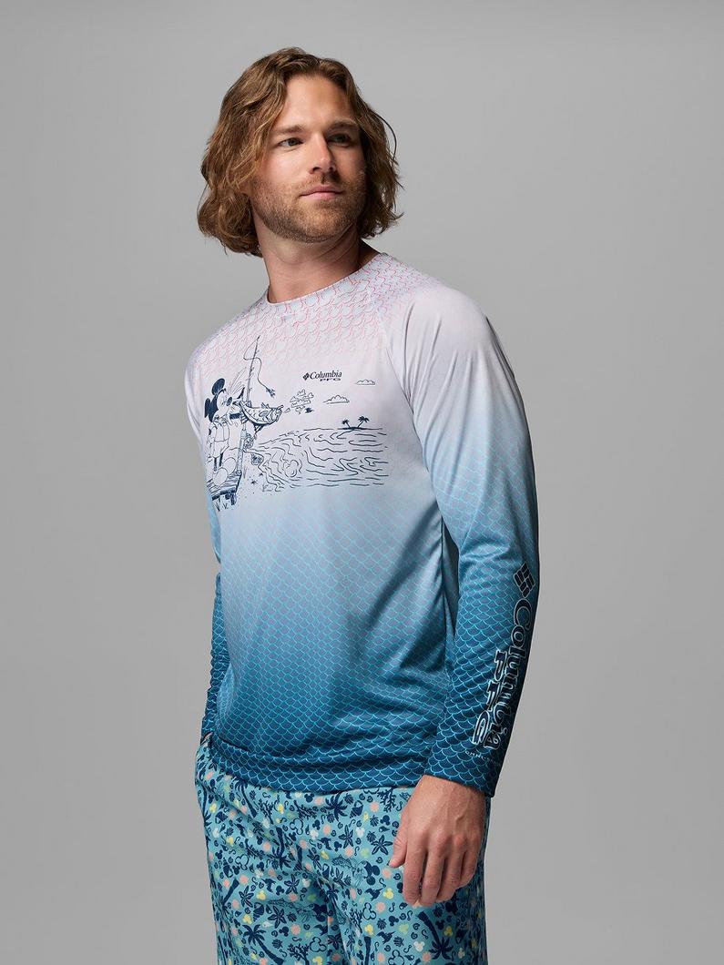 Man wearing long-sleeve performance shirt with fishing scene graphic and blue ombre fish scale pattern.