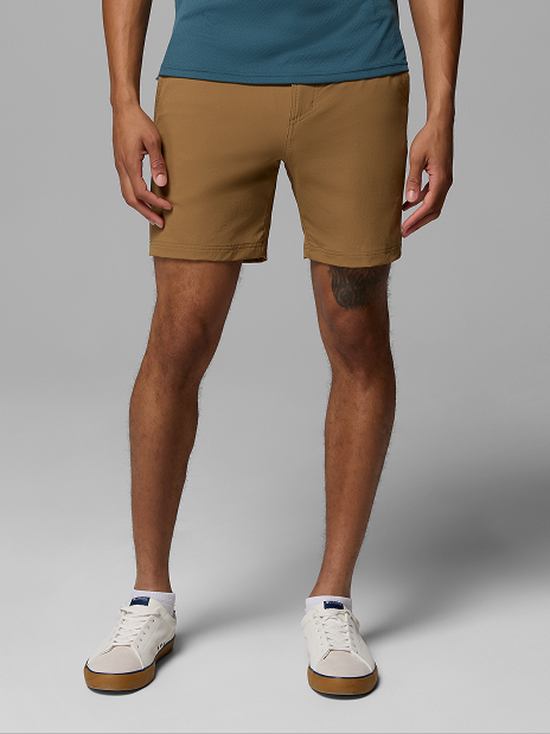 Man wearing tan chino shorts with a teal t-shirt and white sneakers, standing with hands at sides.