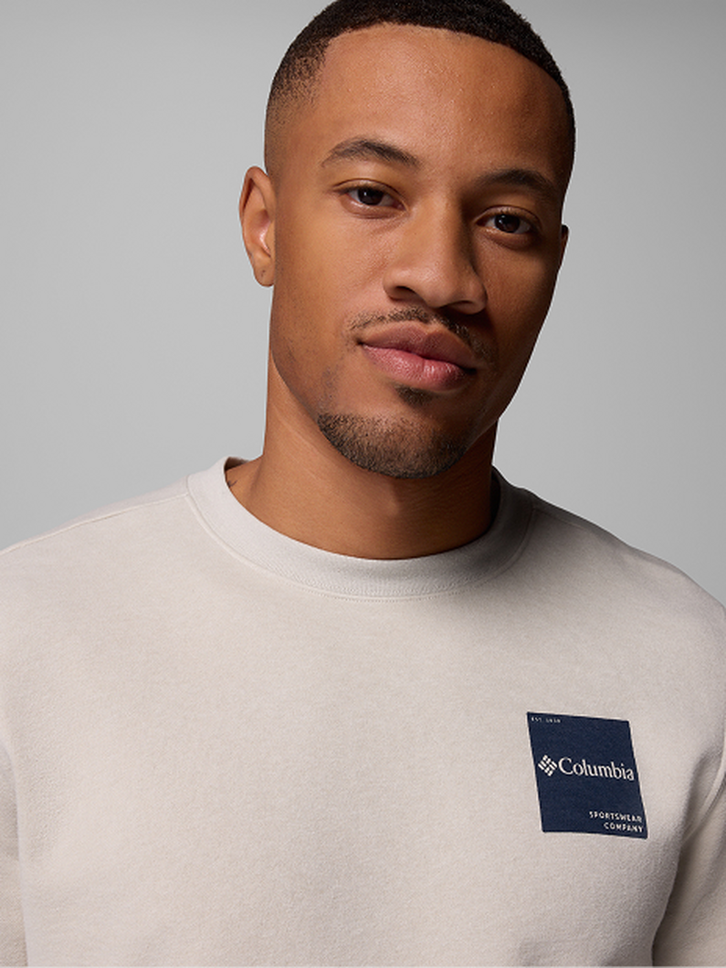 Man wearing a beige crew neck sweatshirt with a small chest patch.
