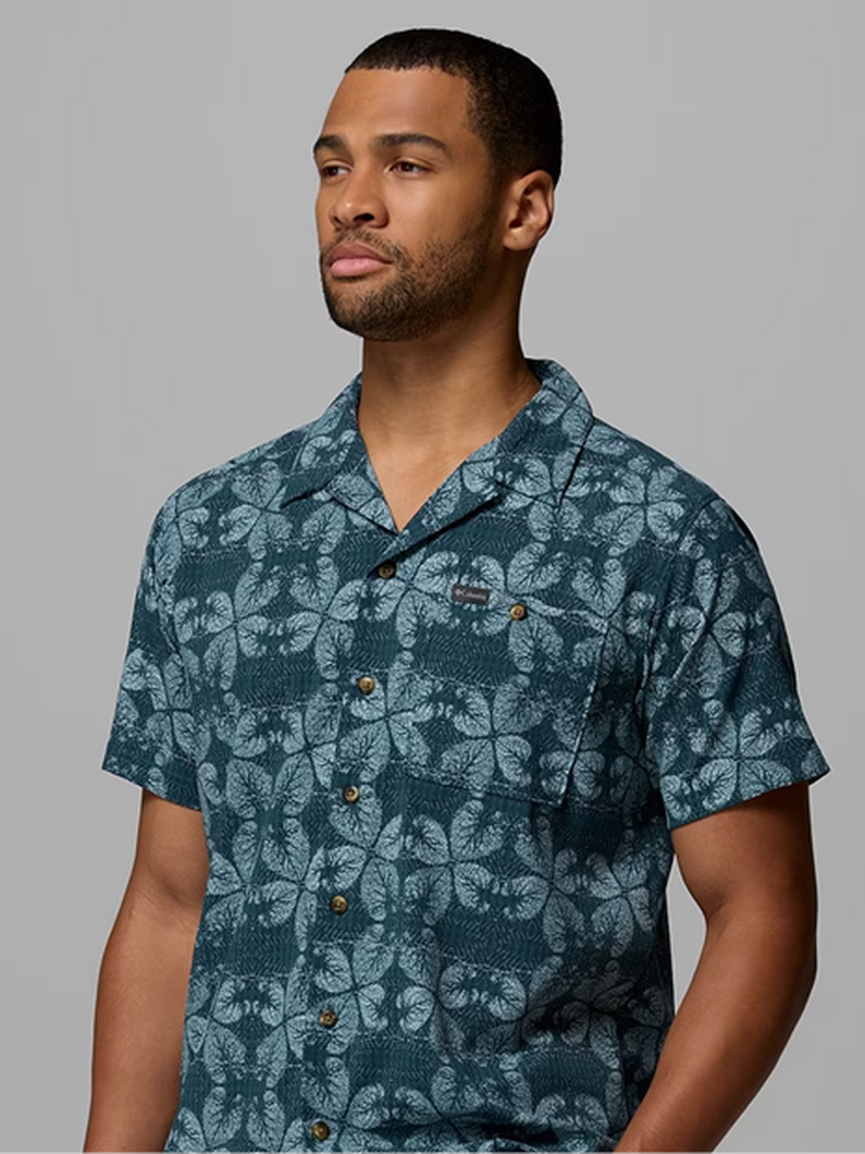 Man wearing a teal short-sleeve button-up shirt with a light blue tropical leaf print pattern.