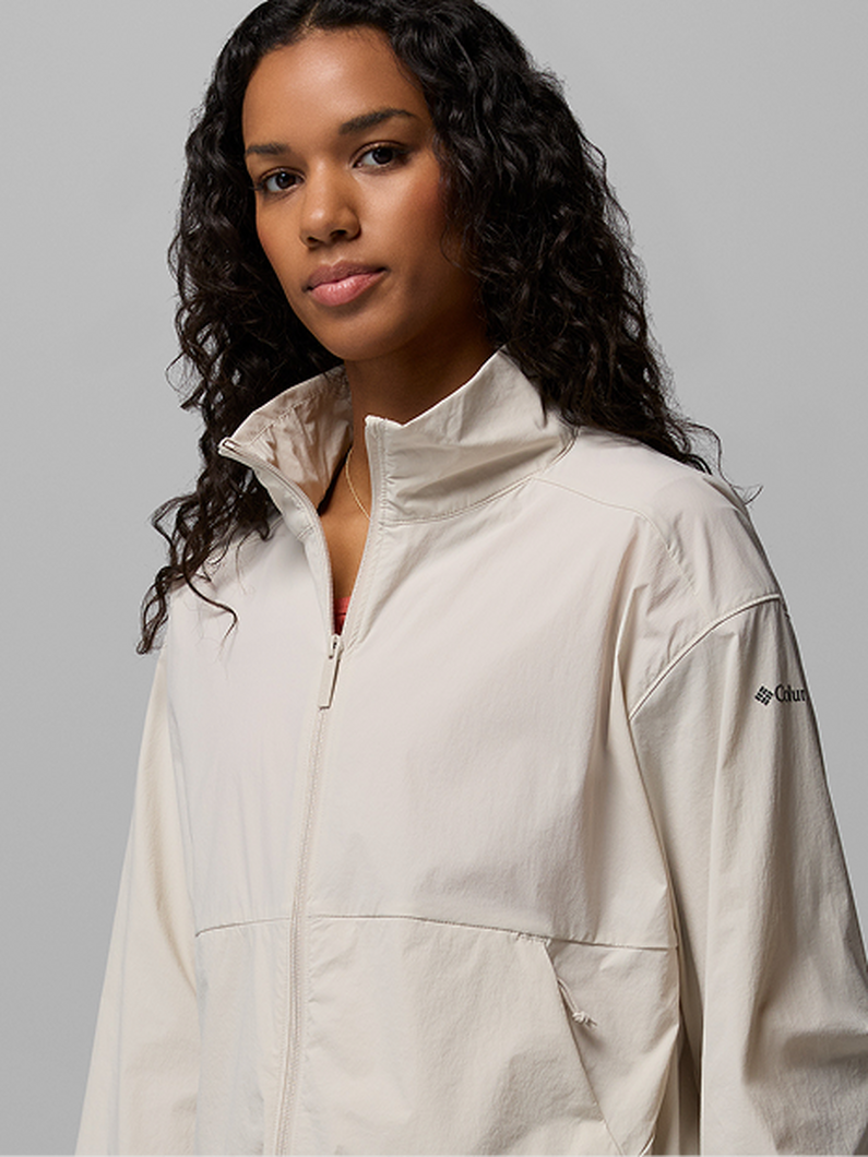 Woman wearing a cream zip-up athletic jacket with stand collar and front pockets.