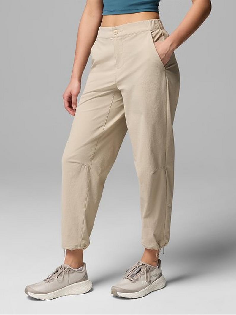 Woman wearing beige high-waisted pants with hand in pocket, paired with blue crop top and athletic shoes.