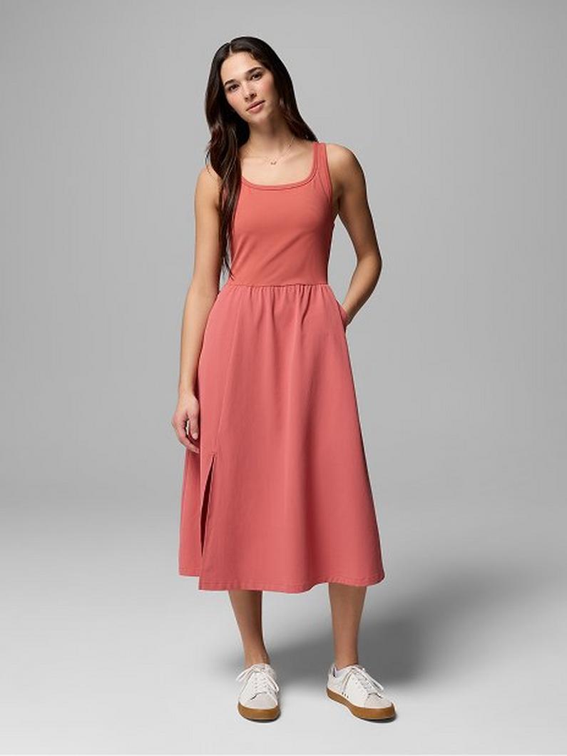 Woman wearing coral sleeveless midi dress with pockets and white sneakers.