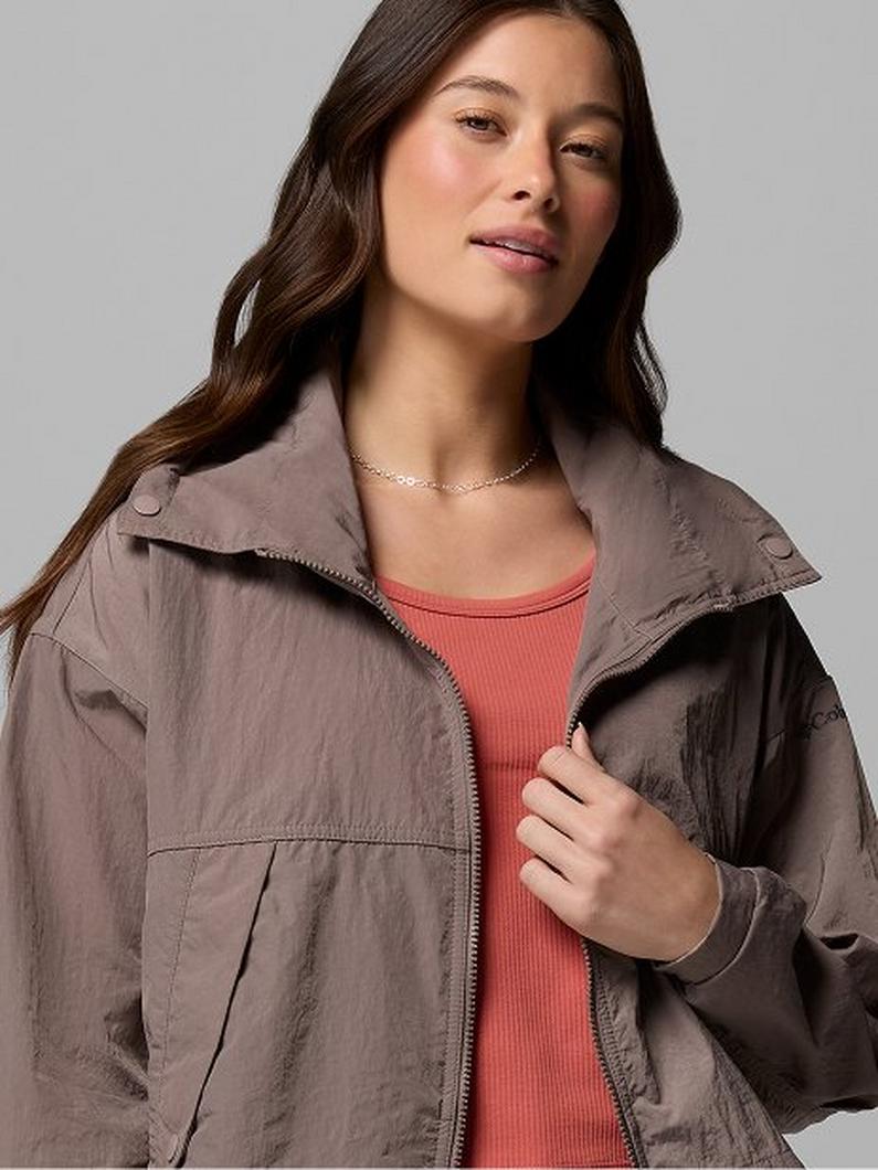 Woman wearing taupe utility jacket with coral top and gold chain necklace.