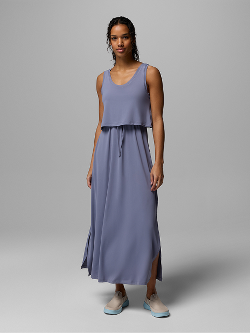 Woman wearing a periwinkle blue sleeveless maxi dress with overlay top, drawstring waist, and side slit.