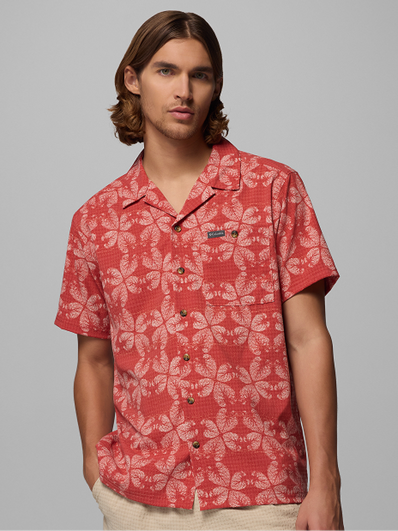 Man wearing coral red short-sleeve camp collar shirt with white tropical leaf print pattern.