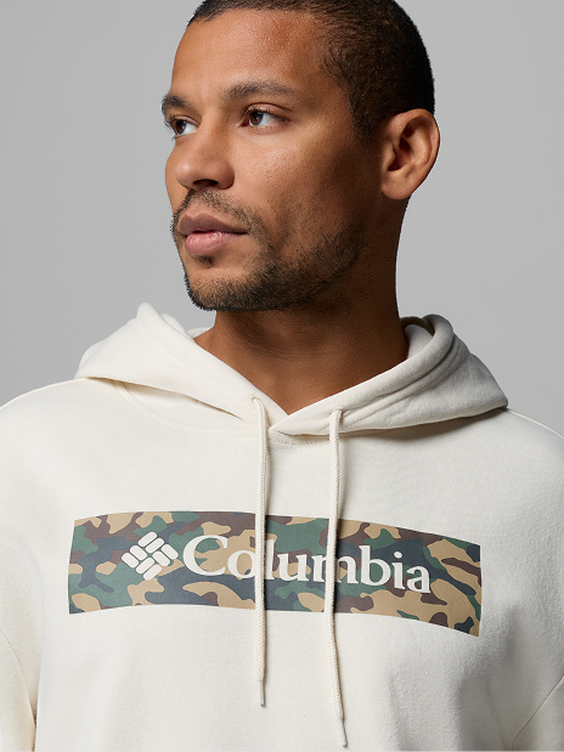 Man wearing cream hoodie with camouflage panel across chest looking to the side.