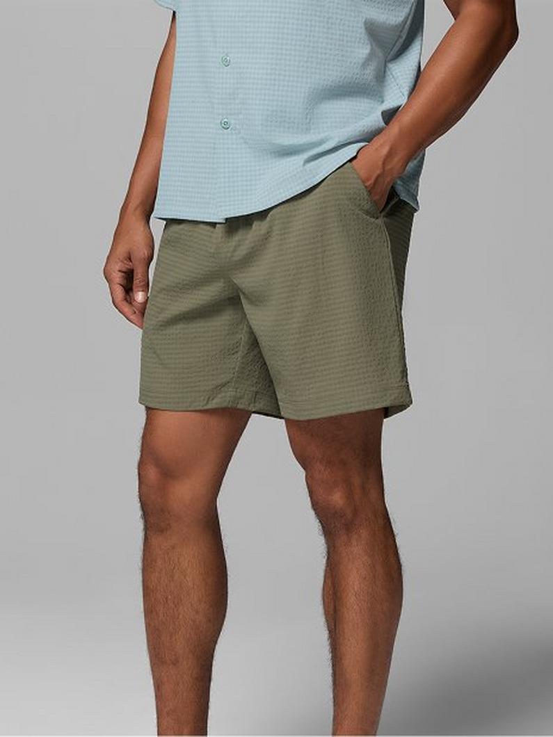Man wearing light blue short-sleeve shirt with hand in pocket of olive green textured shorts.