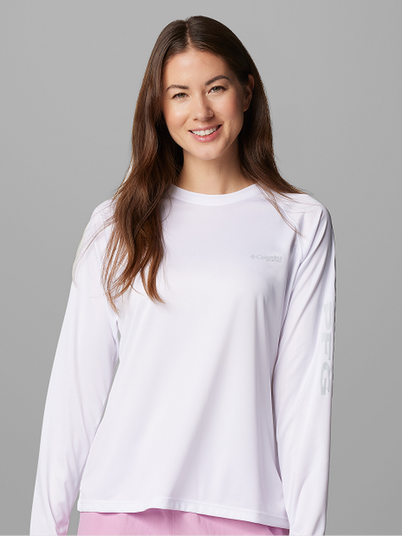 Woman wearing a white long-sleeve athletic shirt with crew neckline, smiling at camera.