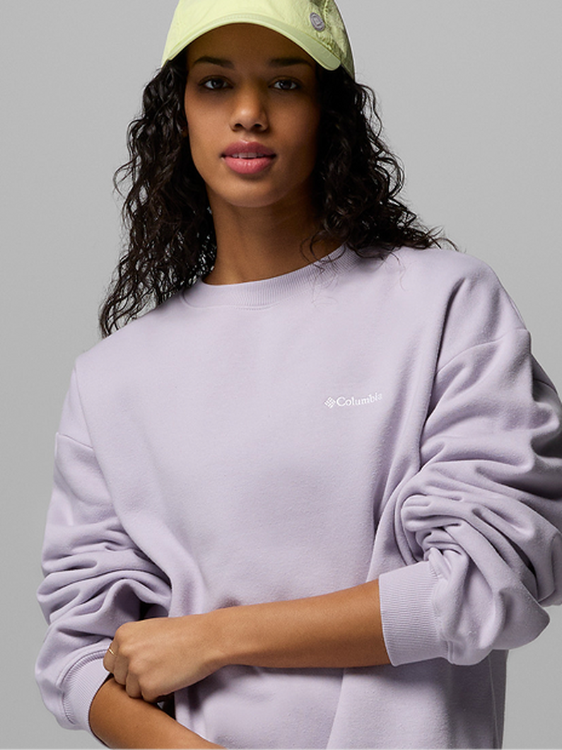 Woman wearing a light purple oversized crewneck sweatshirt and yellow baseball cap.