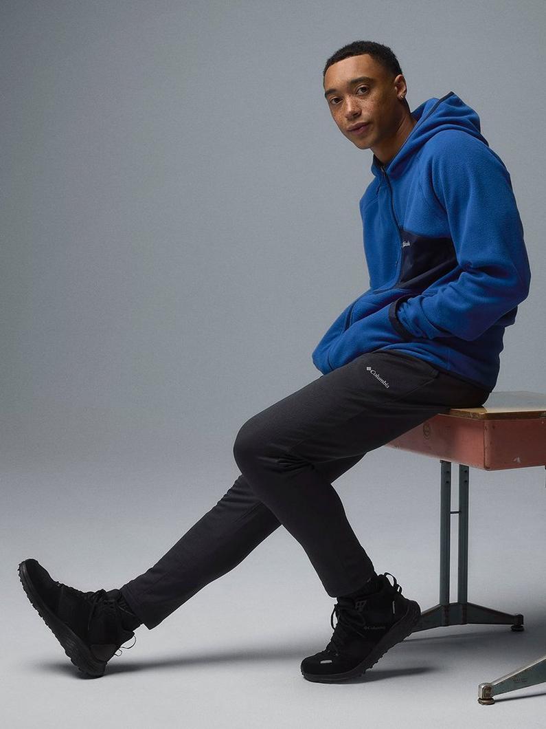 A man sitting on a school desk wearing a blue hoodie.