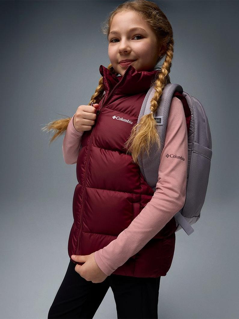 A girl wearing a red puffer vest and backpack.