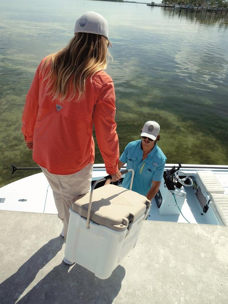 Women in orange fishing shirt loading an ice chest on a boat.
