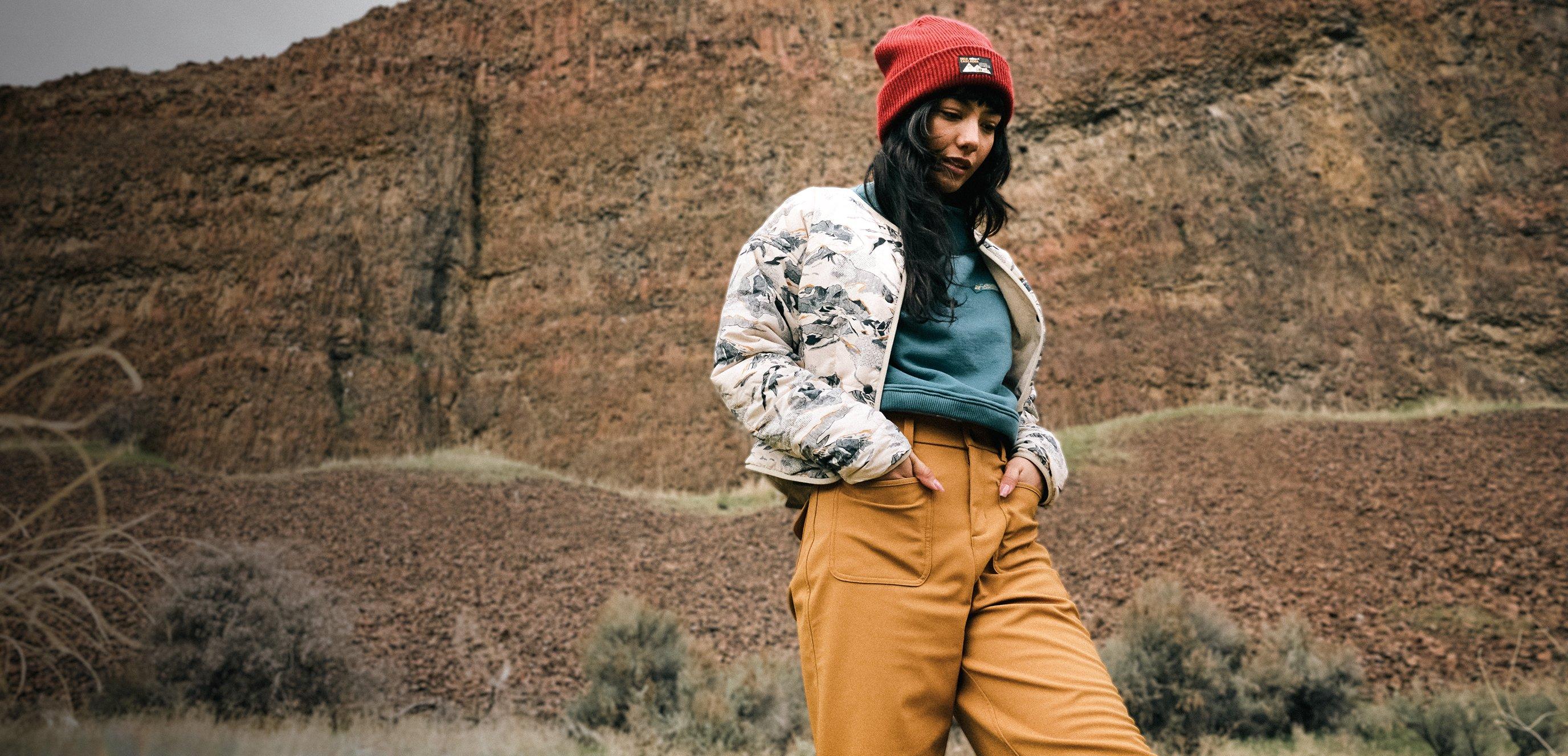 A woman hiking in a beanie and jacket with a rocky landscape in the background.