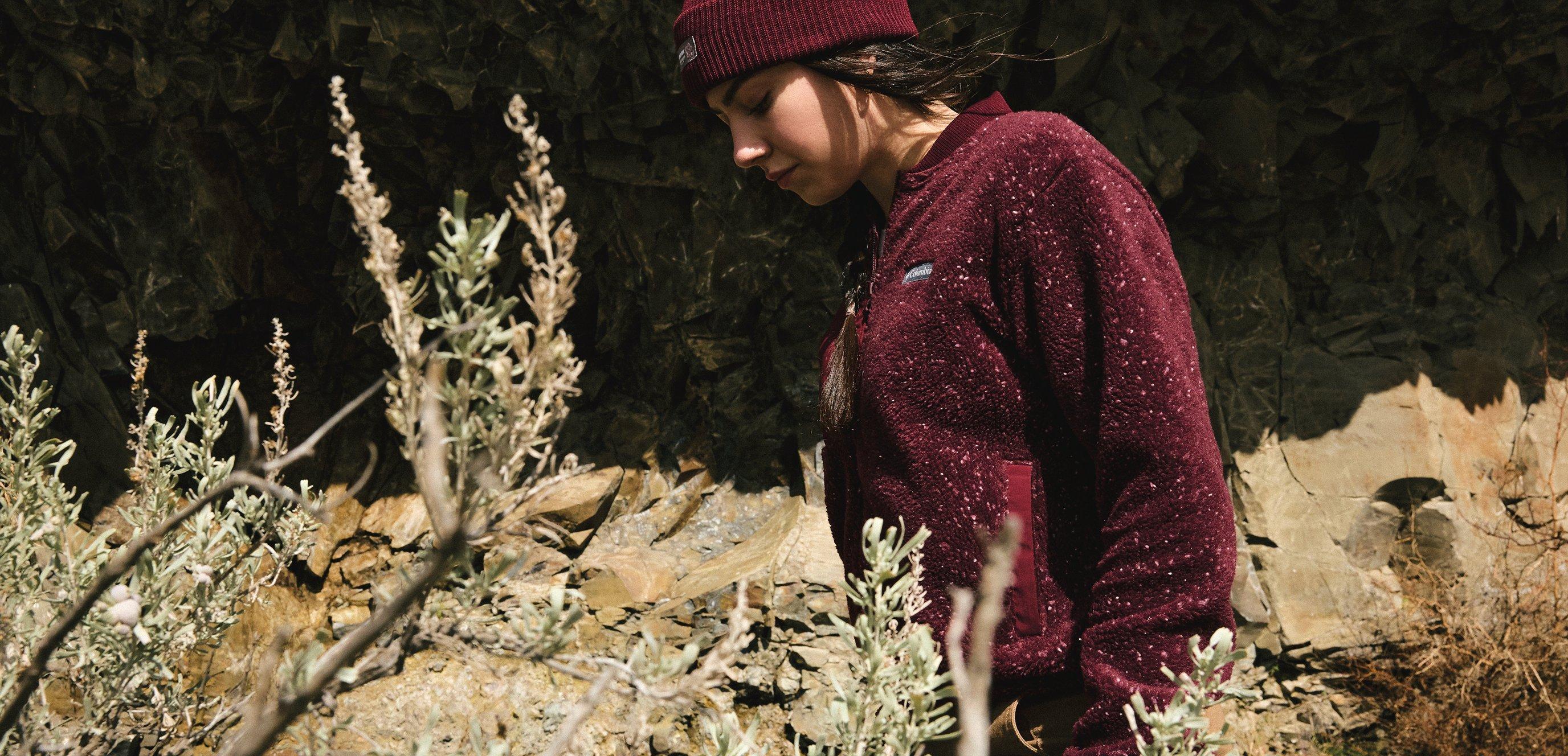 A woman hiking in a fleece in beanie with a rocky landscape in the background.