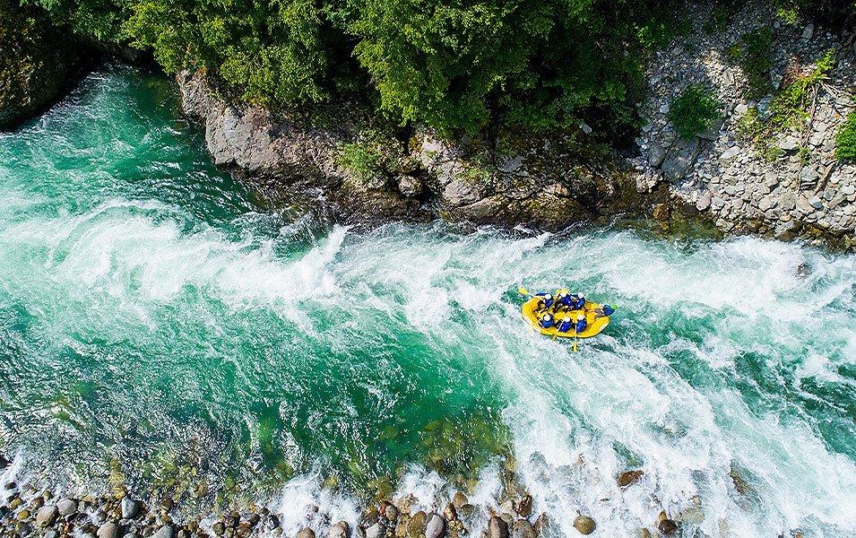 A yellow raft surges through a frothy section of whitewater as the river narrows.