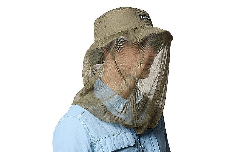 A man wears a brimmed hat with protective netting, dressed for outdoor conditions.