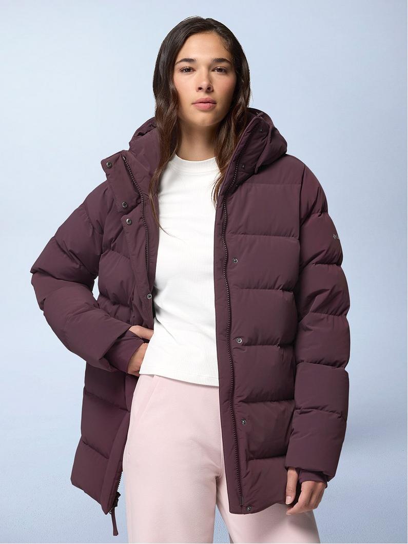 Model wearing burgundy puffer jacket with hood over white sweater and pink pants.