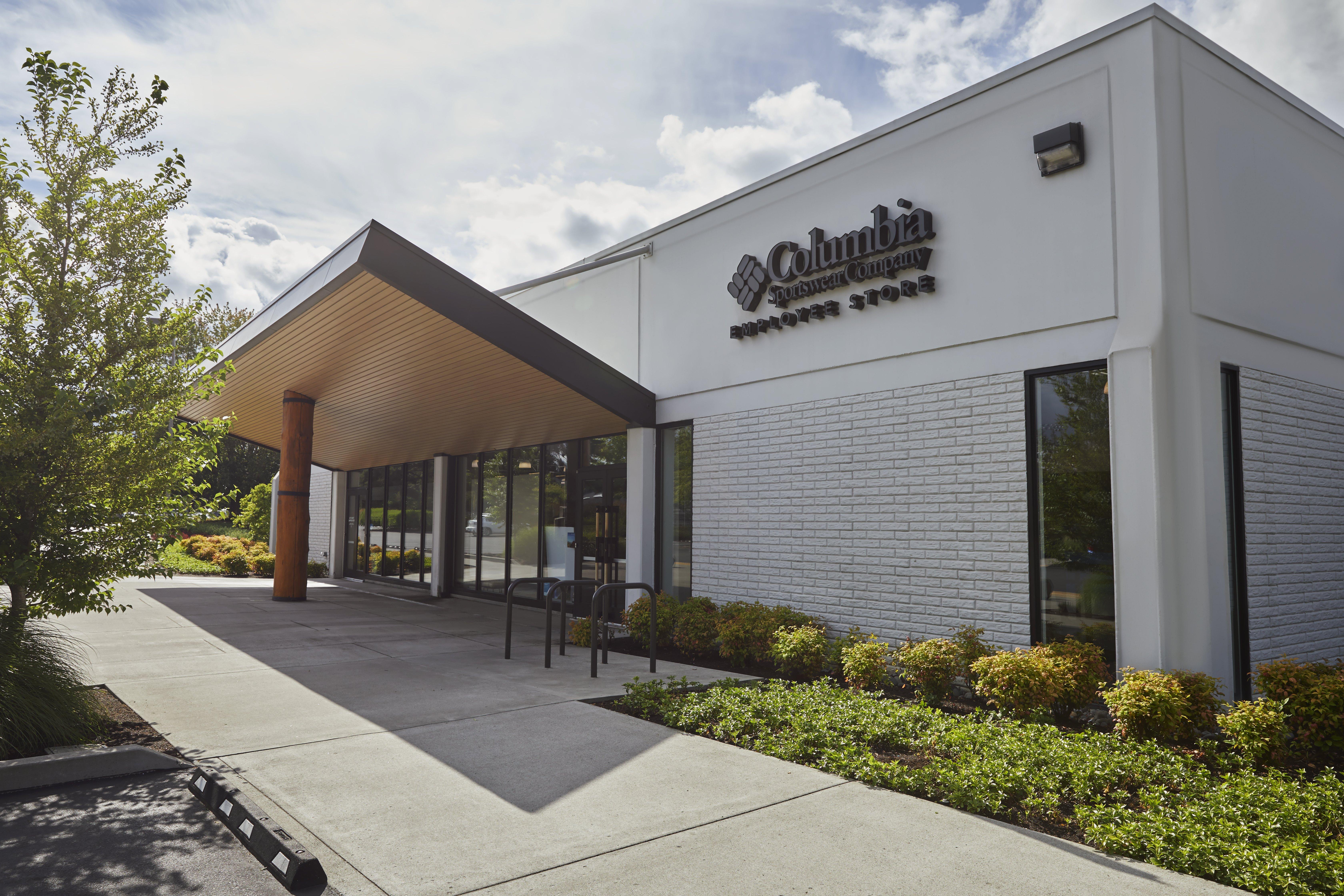 Modern retail store exterior with white brick facade, covered entrance with wood-paneled overhang and glass doors.