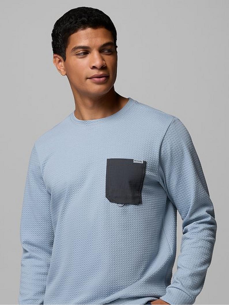 Man wearing light blue textured crew neck long sleeve shirt with contrasting dark gray chest pocket.