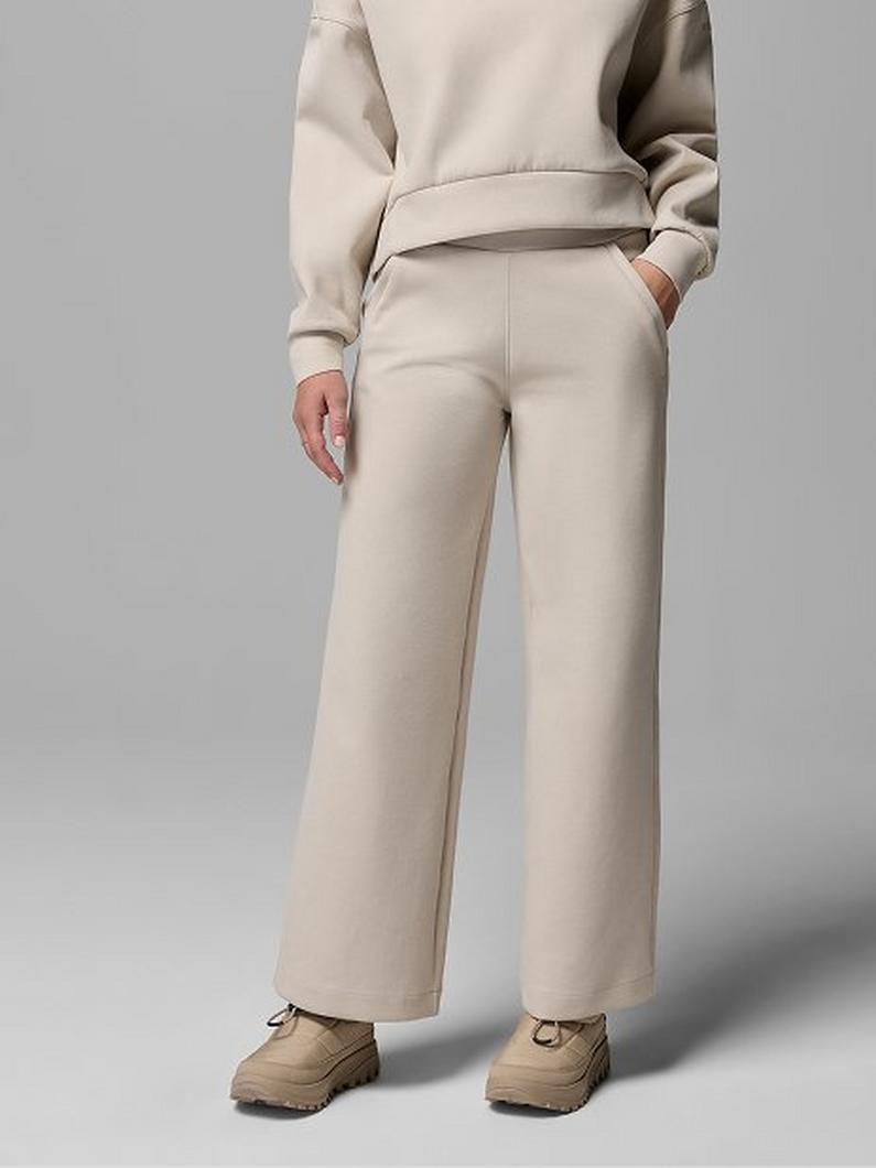 Person wearing beige wide-leg sweatpants with matching sweatshirt and tan lace-up shoes, hand in pocket.