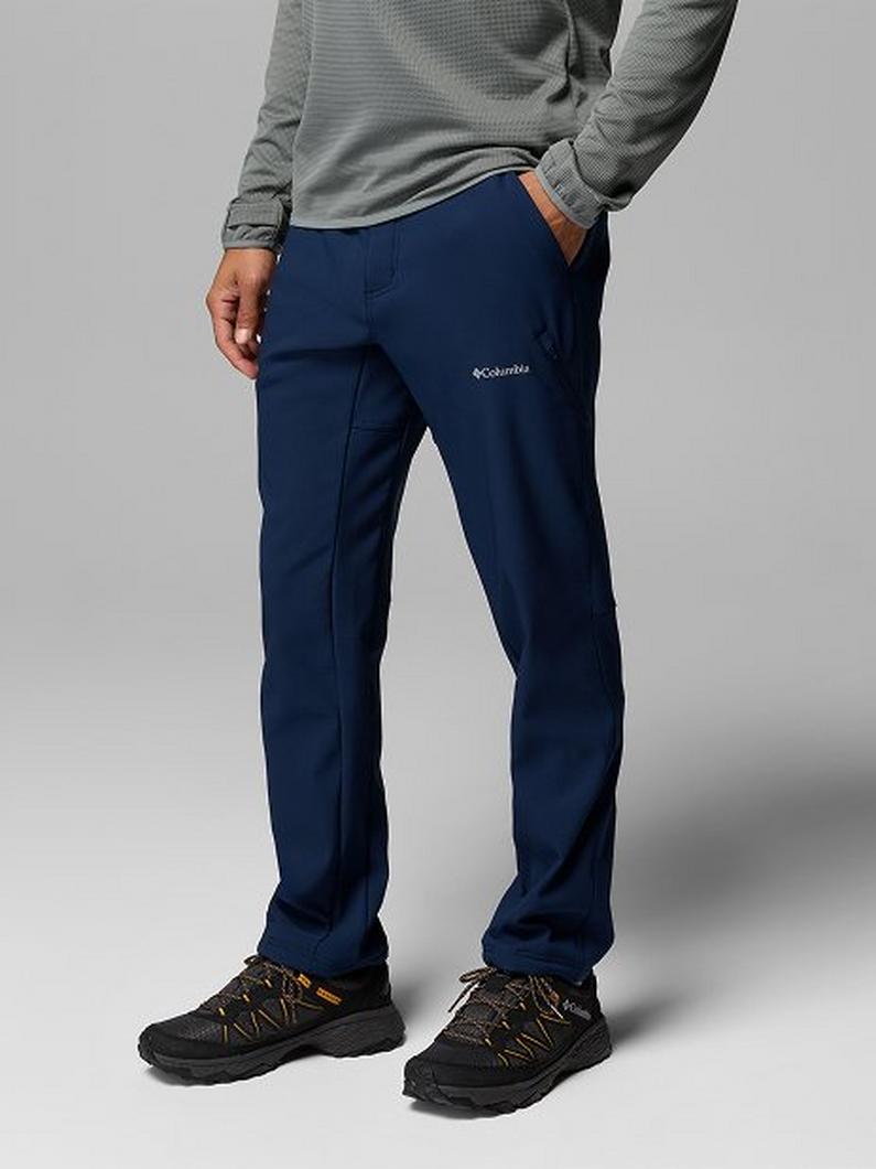Man wearing navy blue outdoor pants with hand in pocket, paired with gray long-sleeve top and hiking shoes.